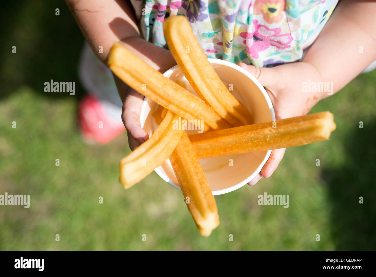 Un gros plan d'une jeune fille dans une jolie robe à fleurs tenant une tasse de papier rempli de churros, beignets frits sticks avec cin Banque D'Images