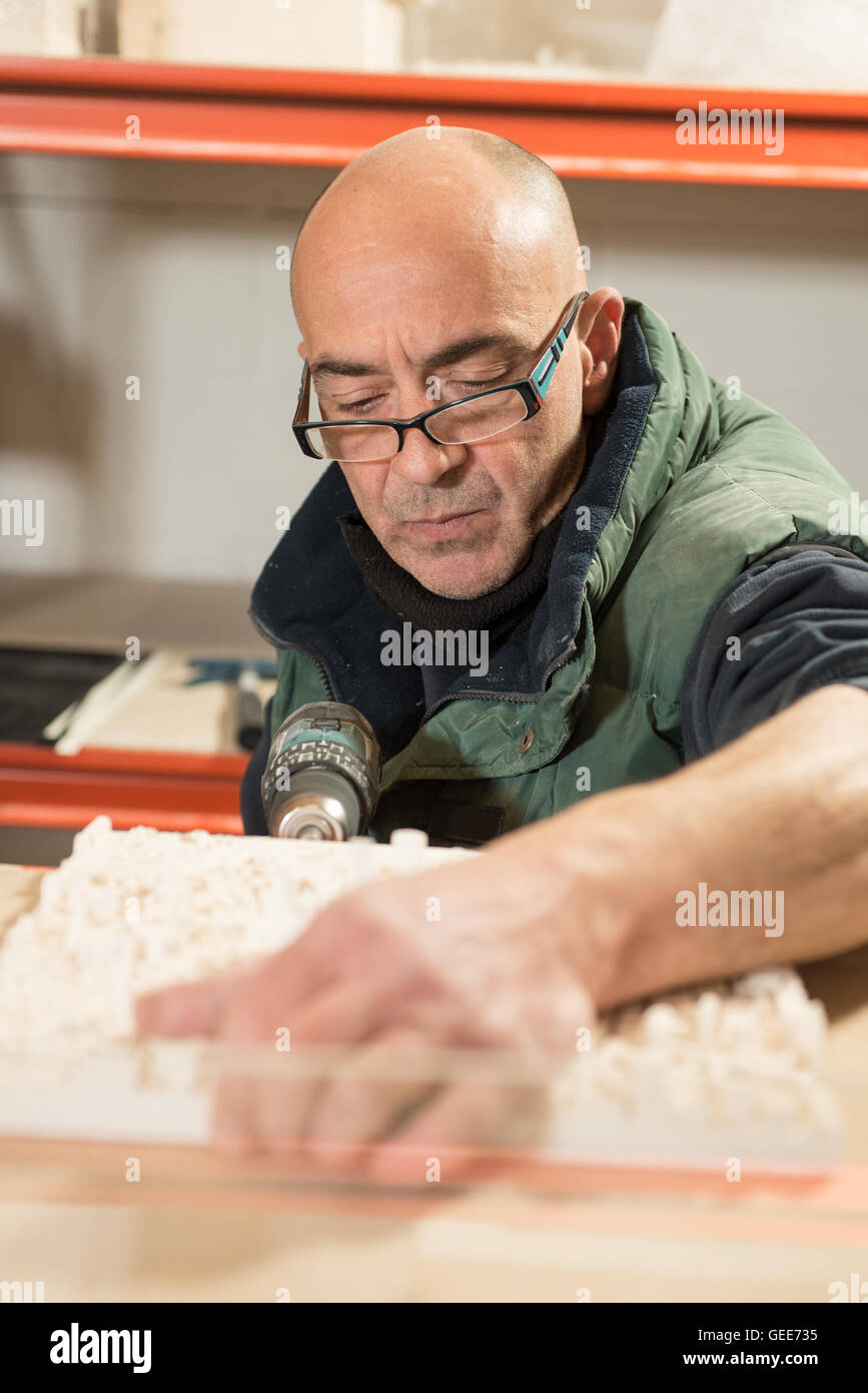 Un homme dans des vêtements épais et lunettes de perforer un côté d'un modèle en plâtre à l'aide d'une perceuse électrique Banque D'Images