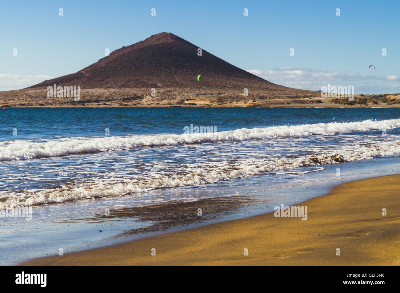 De grosses vagues et du sable jaune-brun sur Playa El Medano beach, Montana Roja montagne sur fond flou, Tenerife, Îles Canaries Banque D'Images