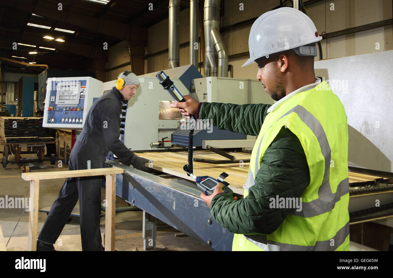 Un ingénieur de l'environnement surveille les niveaux de poussière à côté d'une machine de coupe de bois dans une usine de fabrication au Royaume-Uni. Banque D'Images