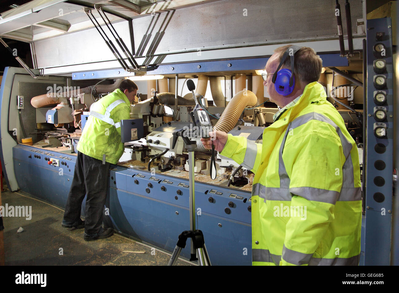 Un ingénieur de l'environnement surveille les niveaux de bruit à côté d'une machine de coupe de bois dans une usine de fabrication au Royaume-Uni Banque D'Images