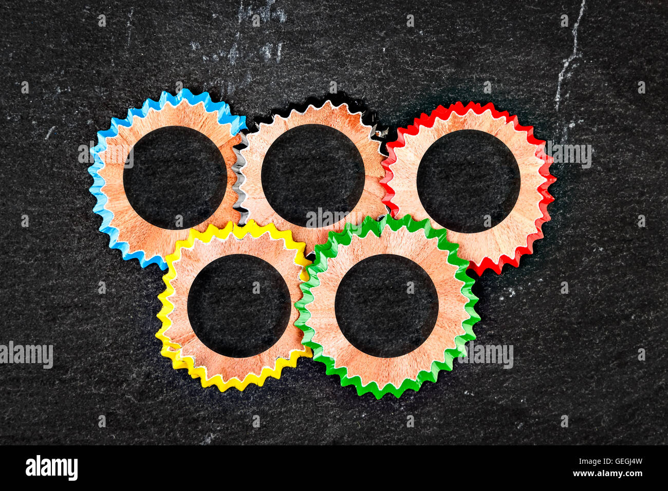 Symbole des anneaux olympiques faits avec des copeaux de crayon de couleur sur une pierre de l'ardoise. Image horizontale. Banque D'Images