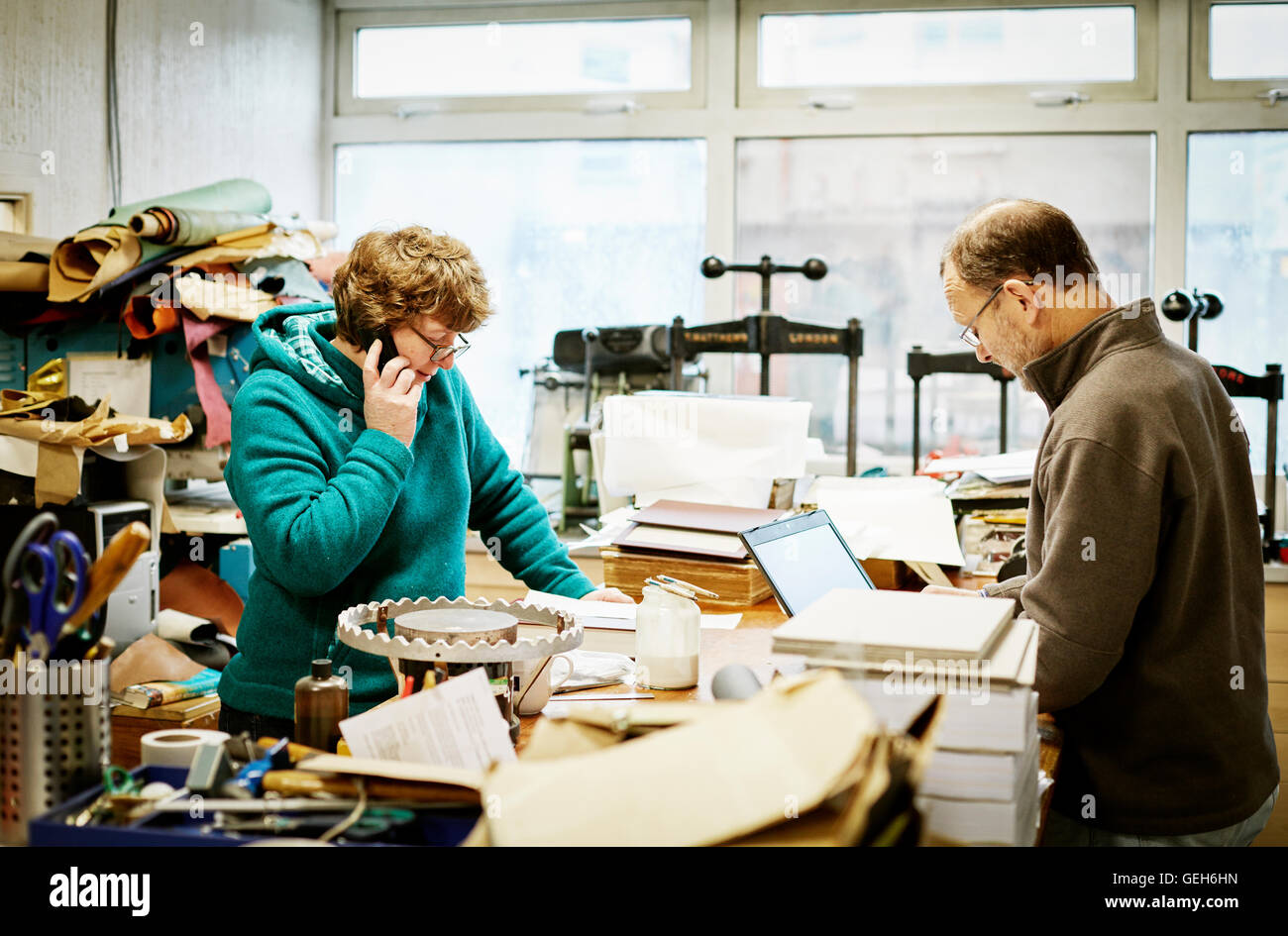Une femme de prendre un appel téléphonique et d'un homme travaillant sur un ordinateur portable dans un atelier de reliure. Banque D'Images