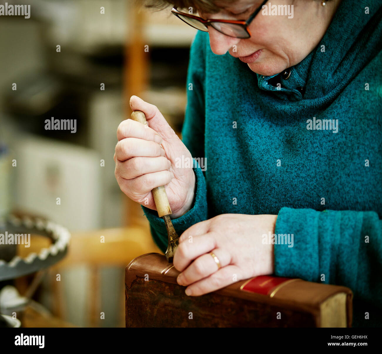 Une femme travaillant sur le dos d'un livre relié avec un outil à main. Banque D'Images