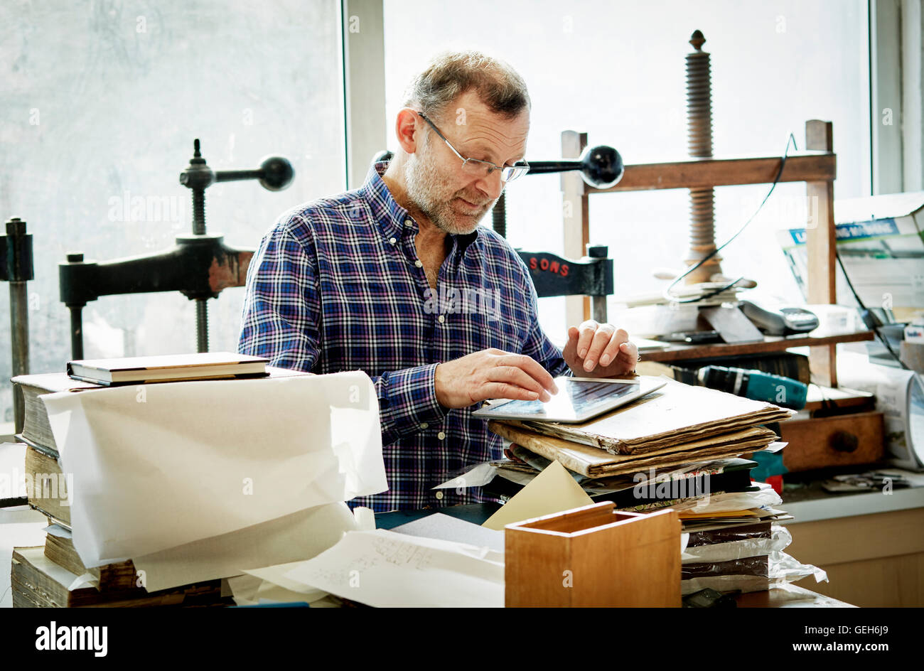 Un homme à l'aide d'une tablette numérique dans un atelier de reliure. Banque D'Images