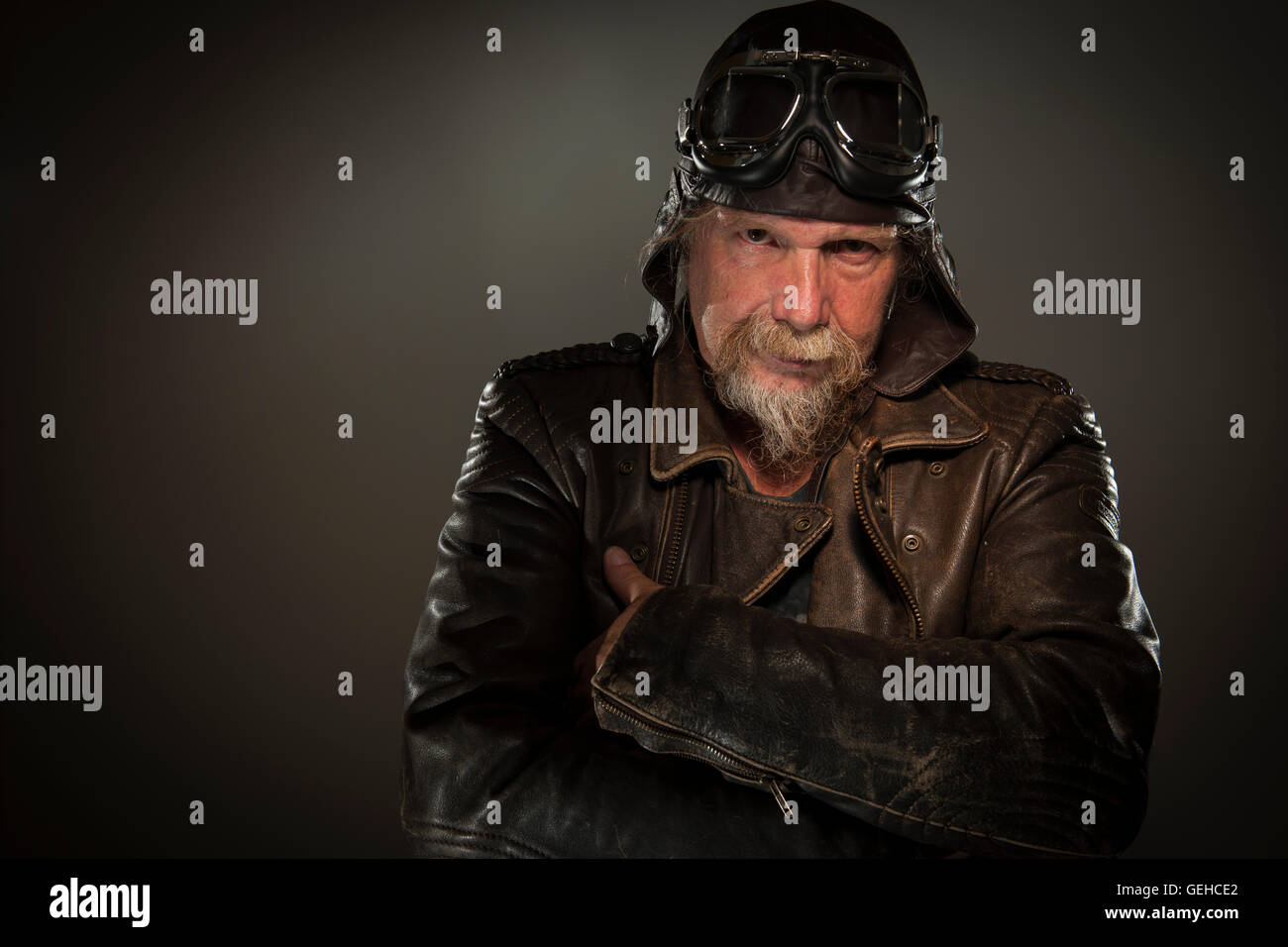 Tête et épaules frontal portrait de vieil homme avec une barbe complète, blouson de cuir et lunettes au sérieux dans l'appareil photo Banque D'Images