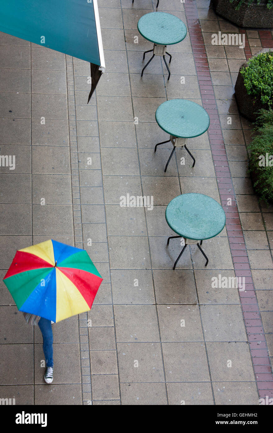 Caffe vide les tables sur un jour de pluie. Quelqu'un qui tient un parapluie en marche. Banque D'Images