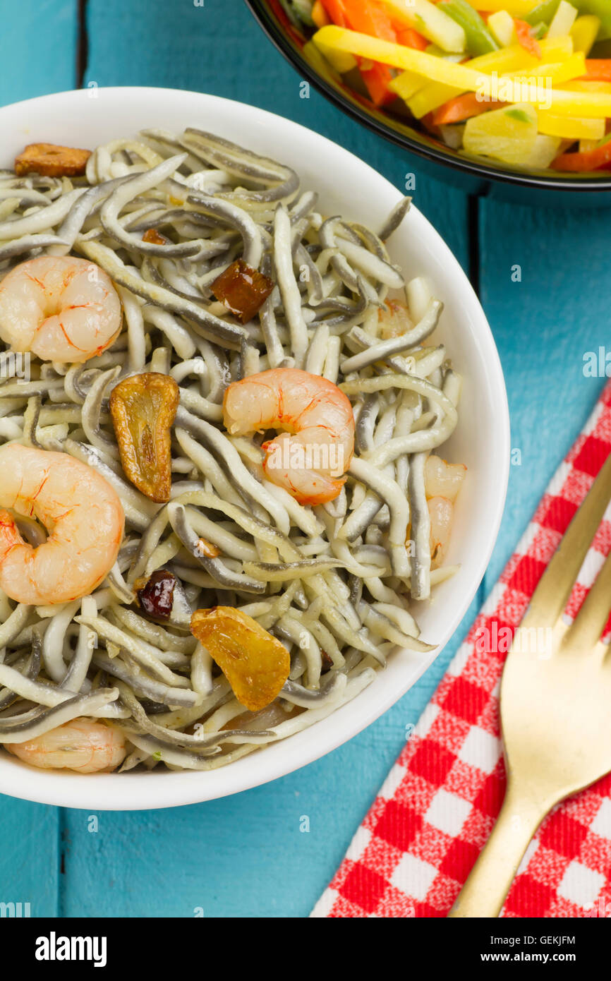 Les civelles Surimi avec les crevettes, l'ail et le poivre dans un bol blanc, des légumes sur une fourche d'or noir bol, sur une serviette rouge Banque D'Images