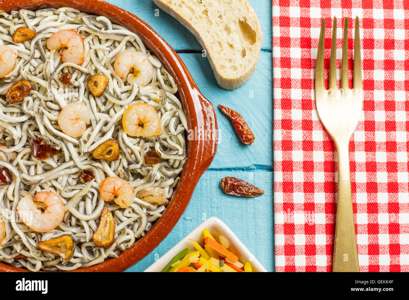 Les civelles Surimi avec les crevettes, l'ail et poivre sur pot en argile, avec une fourche d'or sur une serviette Banque D'Images