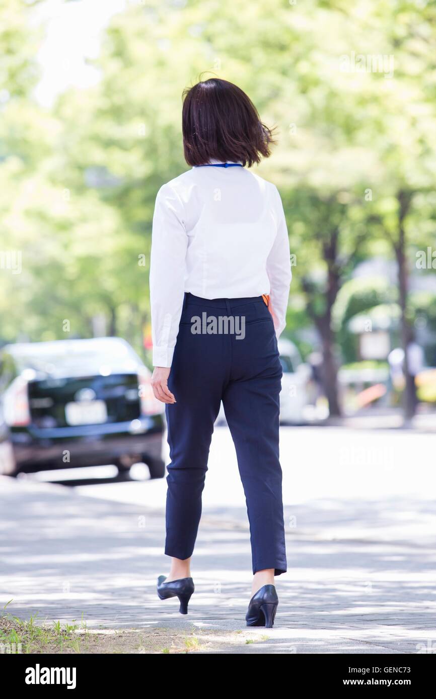 Business Woman walking along avec tree-lined road Banque D'Images