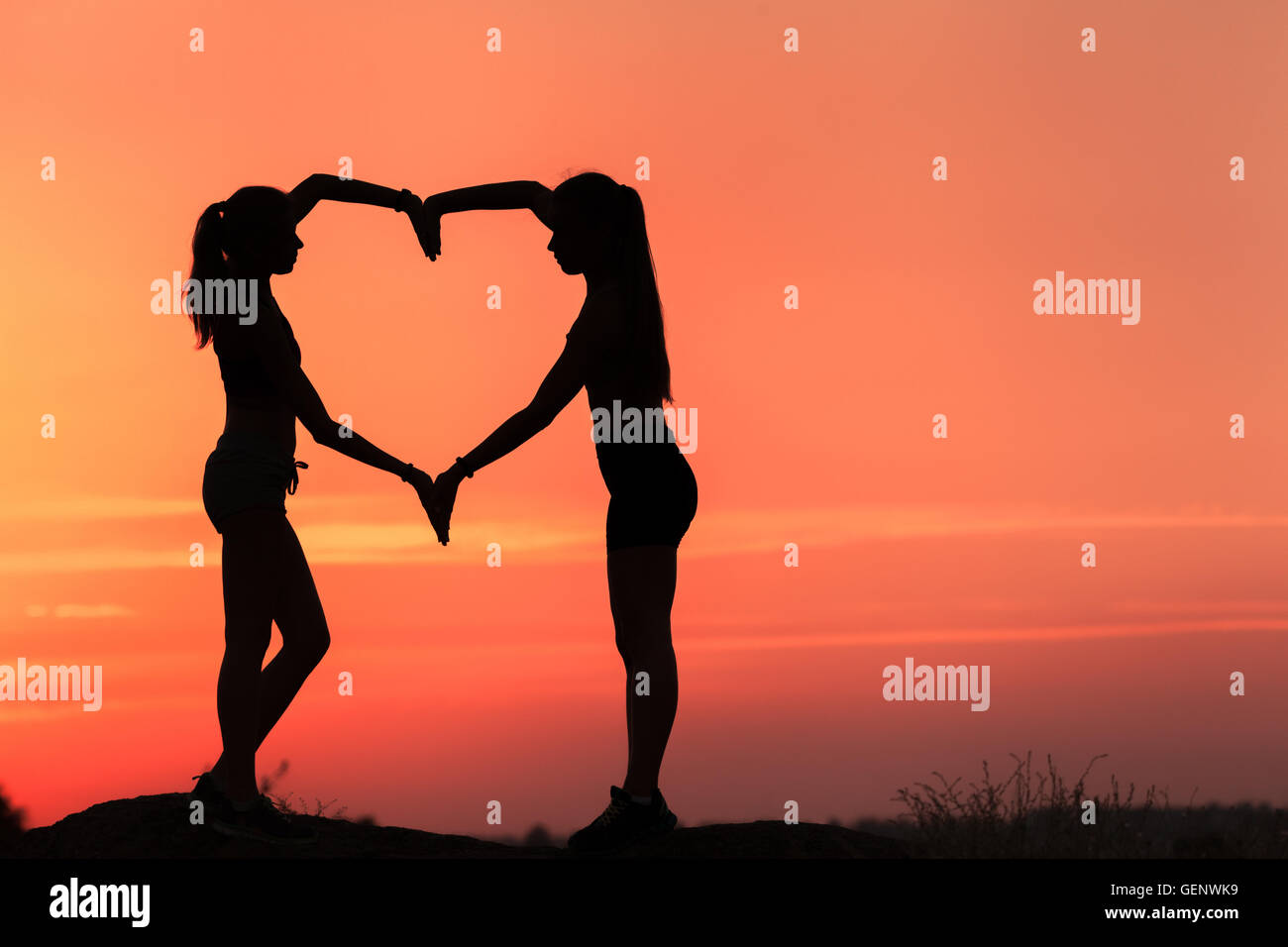 Paysage avec silhouette de young women holding hands en forme de coeur sur le fond de ciel coloré au coucher du soleil Banque D'Images