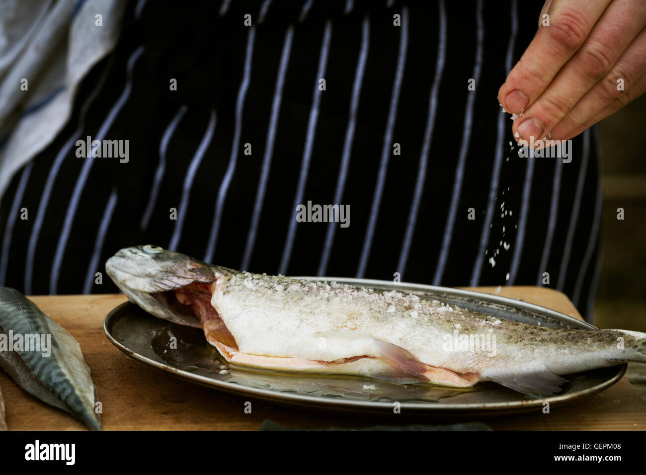 Portrait d'un chef cuisinier sur un sel saupoudrer le poisson frais. Banque D'Images