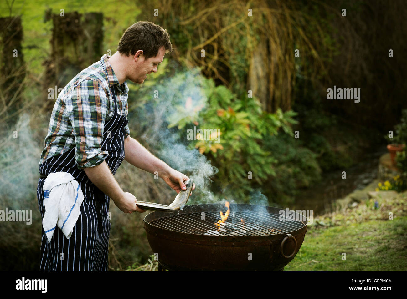 Chef standing in a garden, griller le poisson sur un barbecue. Banque D'Images
