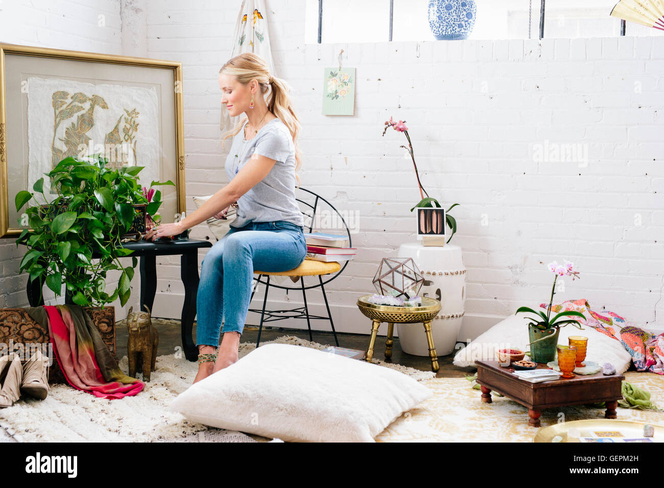 Une jeune femme assise sur une chaise dans un appartement décoré avec des photos et des plantes. Banque D'Images