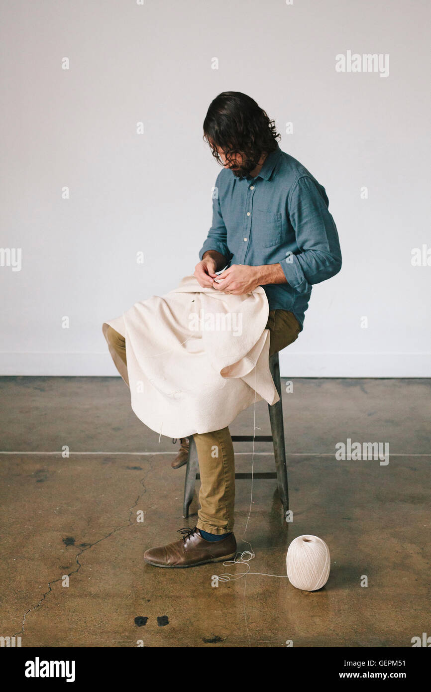 Un homme assis sur un tabouret, avec de la corde et de la main pour créer un exercerez pièce d'art. Banque D'Images