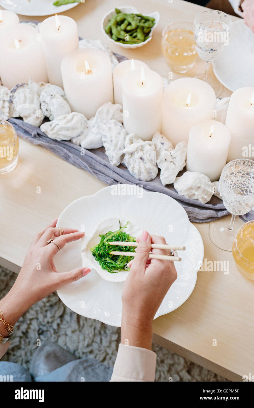 Vue de dessus d'une table avec des bougies et une personne à l'aide de baguettes pour manger des légumes verts. Banque D'Images