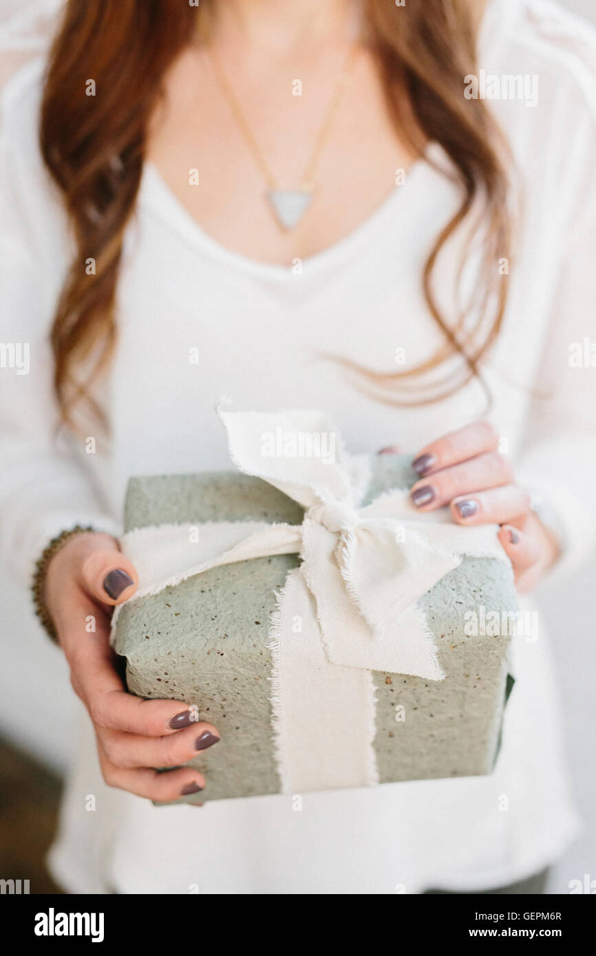 A woman holding a gift wrapped fort avec un large ruban noué dans un arc. Banque D'Images