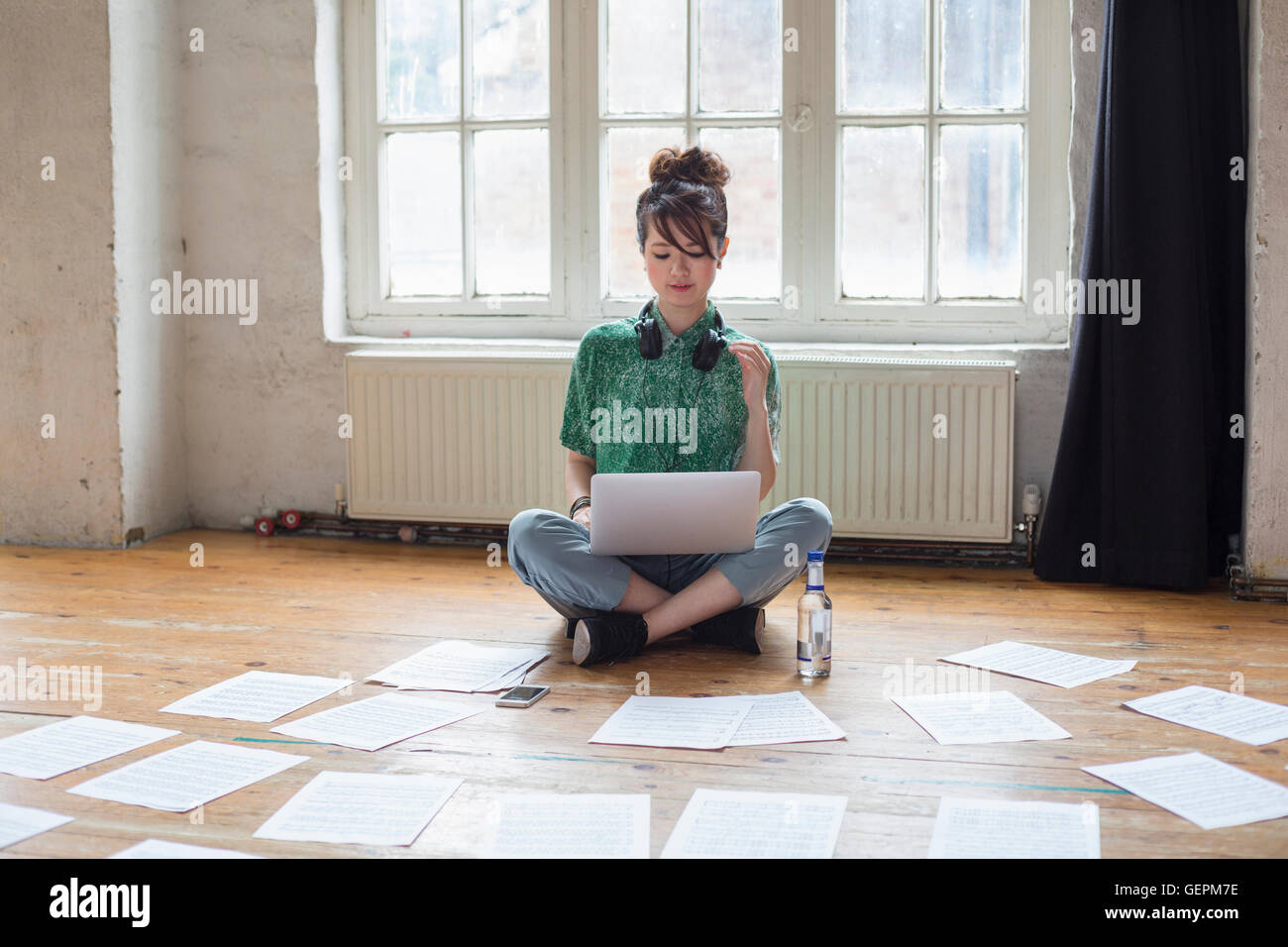 Jeune femme assise sur le sol dans un studio de répétition, à l'aide d'un ordinateur portable, à la recherche de partitions de musique. Banque D'Images