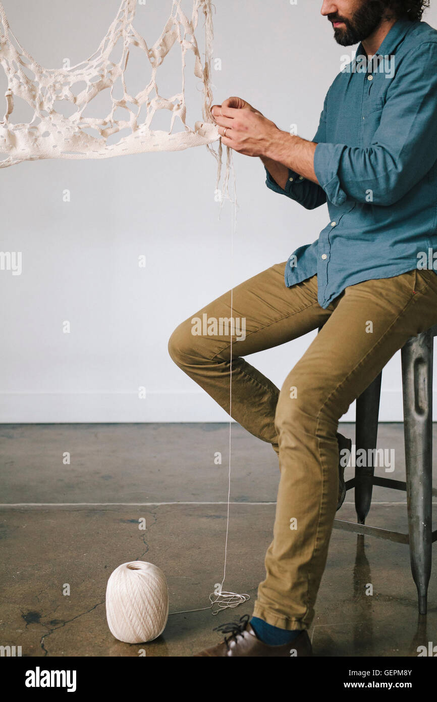 Un artiste assis à travailler sur un morceau d'art, pièces de tissus et de fil. Banque D'Images