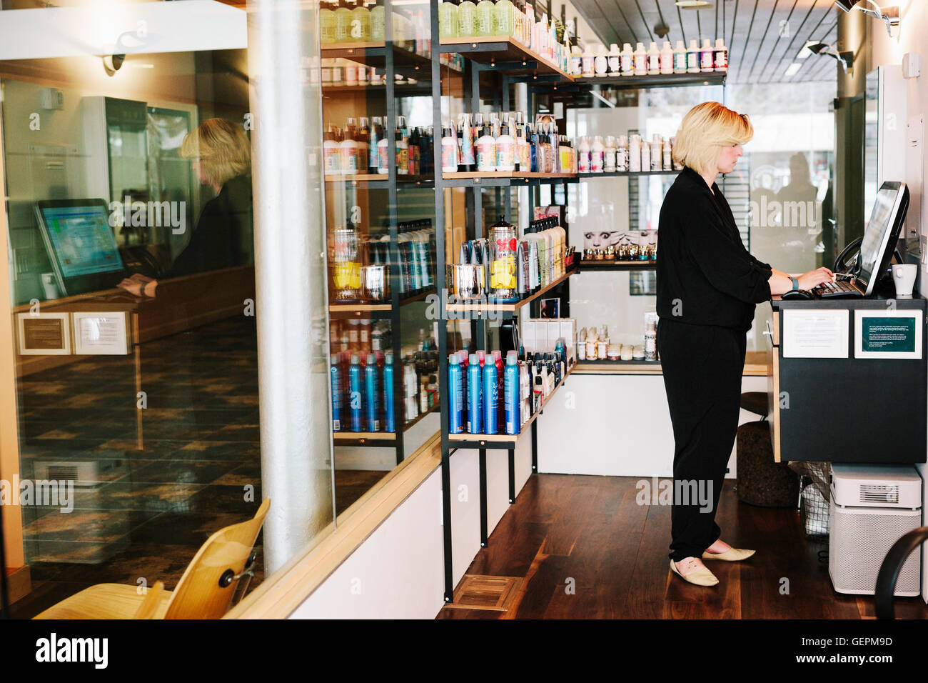 Une femme à l'aide d'un ordinateur portable dans un salon de coiffure, l'accueil, la gestion de l'entreprise. Banque D'Images