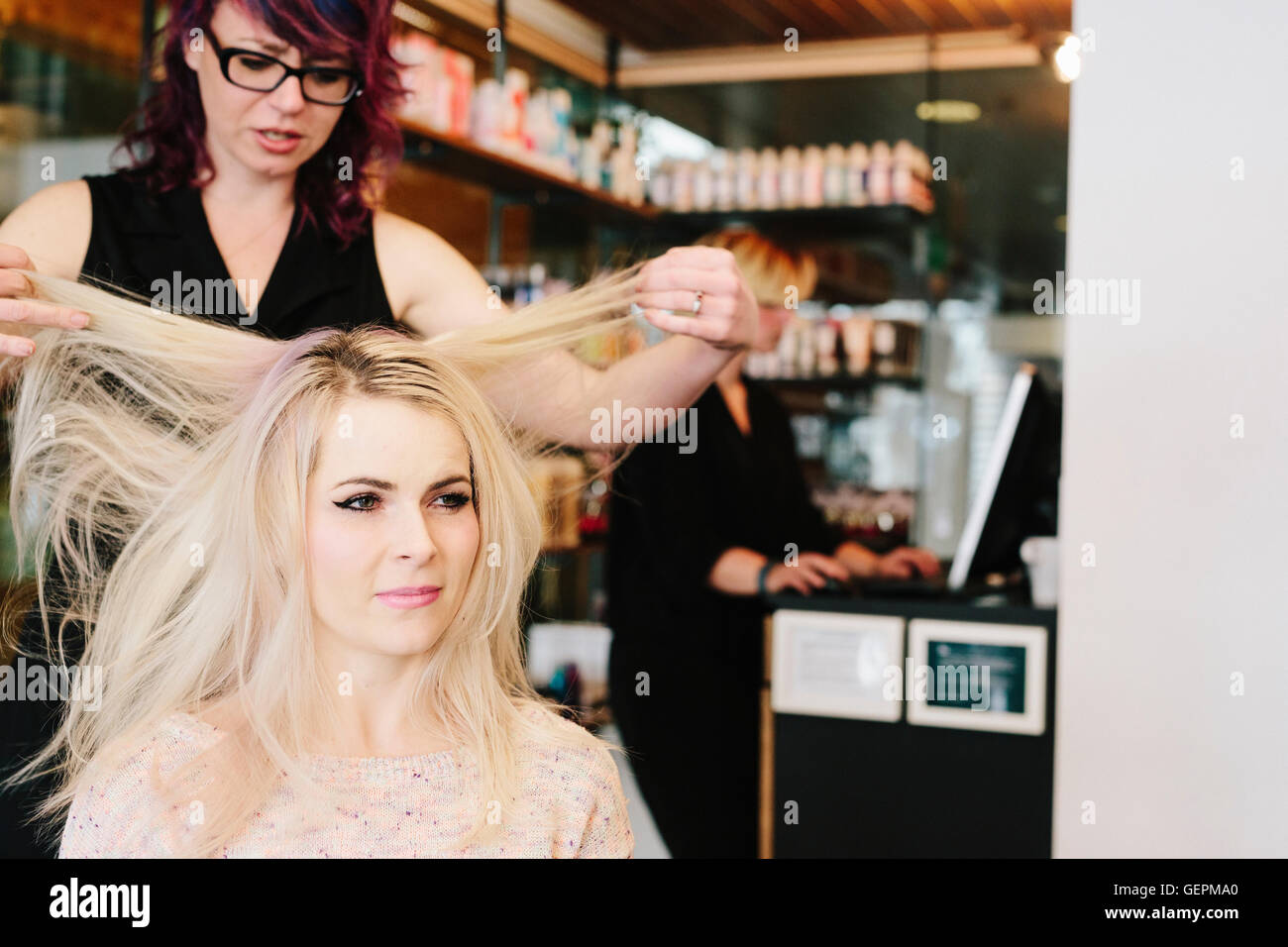 Un coiffeur et un client, une jeune femme avec de longs cheveux blonds, à un salon de coiffure. Banque D'Images