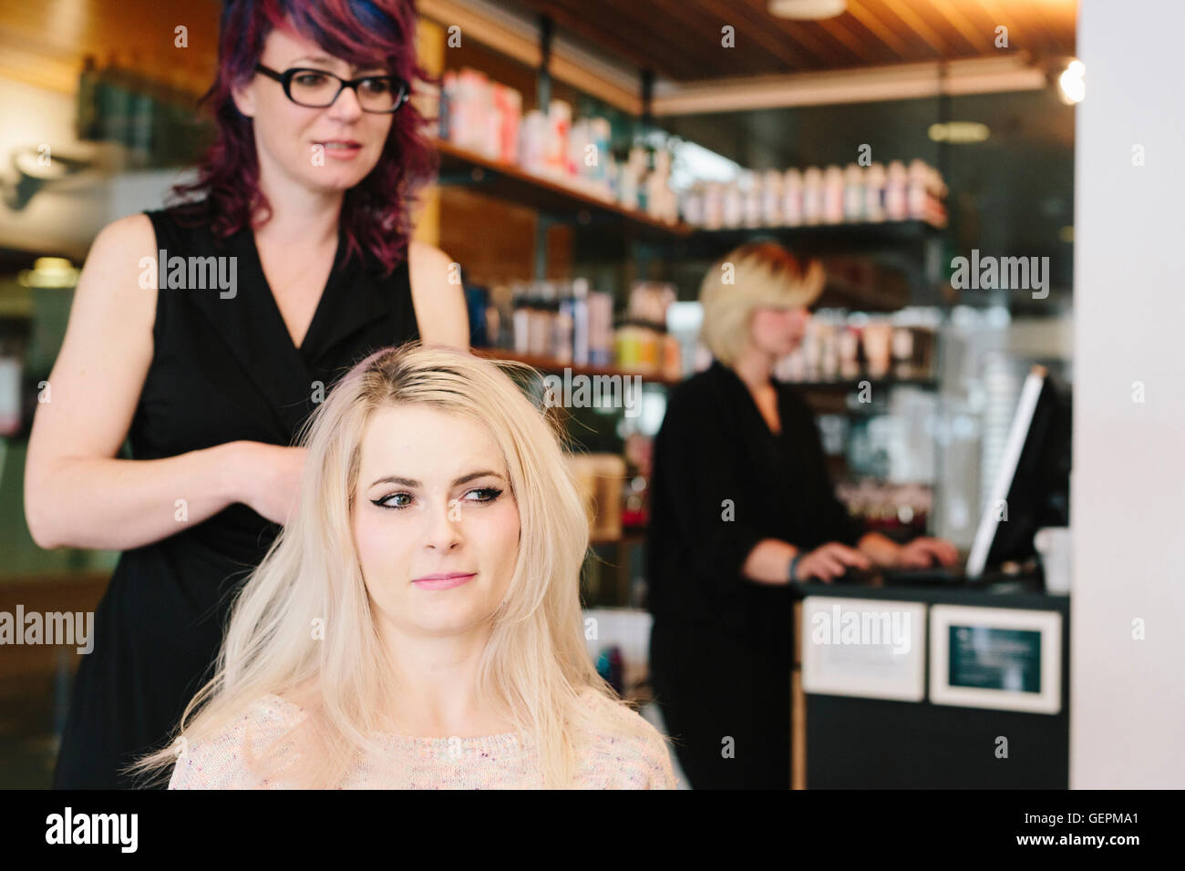 Un coiffeur et un client, une jeune femme avec de longs cheveux blonds, à un salon de coiffure. Banque D'Images