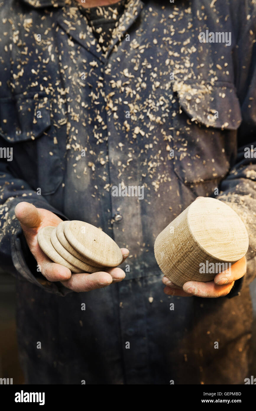 Portrait d'un homme en salopette couverte de sciure, tenant une forme en bois tourné et disques en bois dans ses mains. Banque D'Images