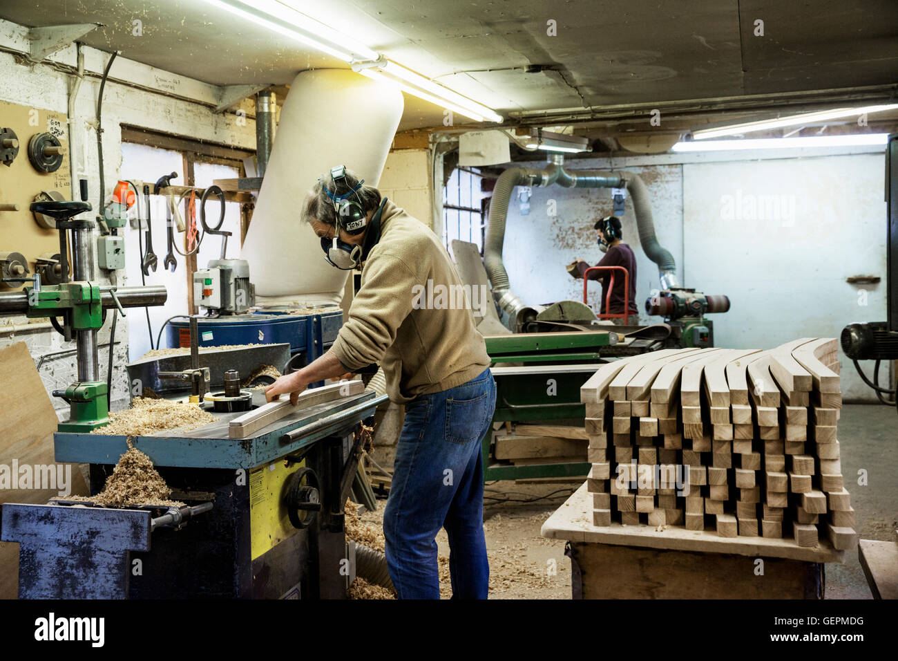 Homme debout dans un atelier de menuiserie, un respirateur et protecteur auditif, de travailler sur un morceau de bois. Banque D'Images