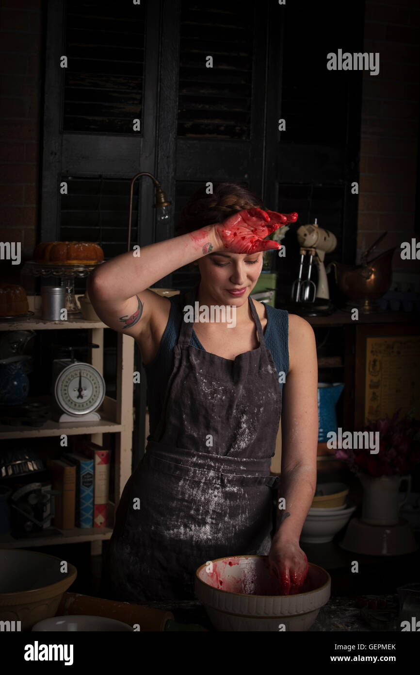 La Saint-Valentin, jeune femme debout dans une cuisine, la préparation de la confiture de framboises, essuyant sa main sur son front. Banque D'Images