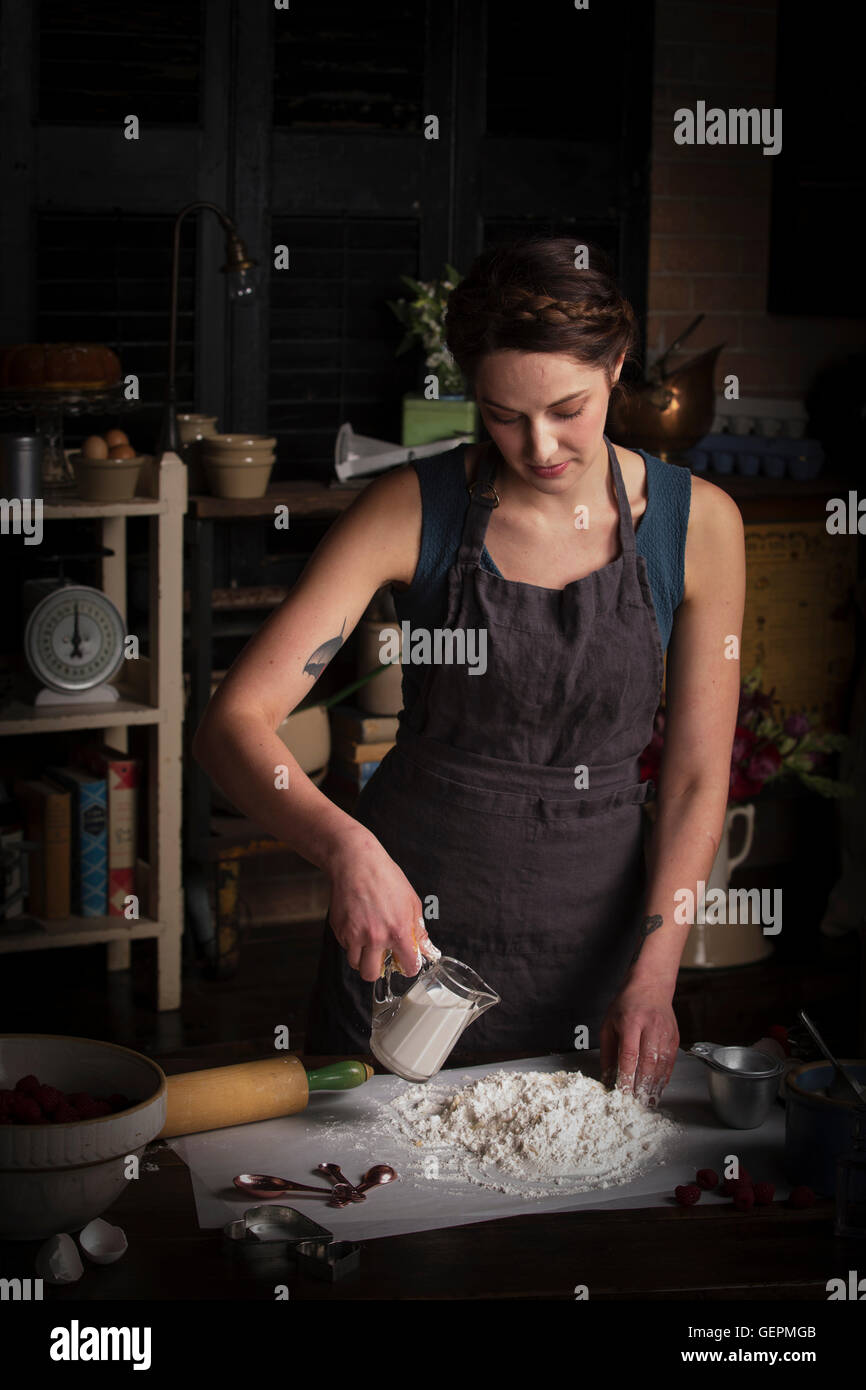 La Saint-Valentin, jeune femme debout dans une cuisine, la préparation de la pâte à biscuits, verser le lait d'une cruche. Banque D'Images