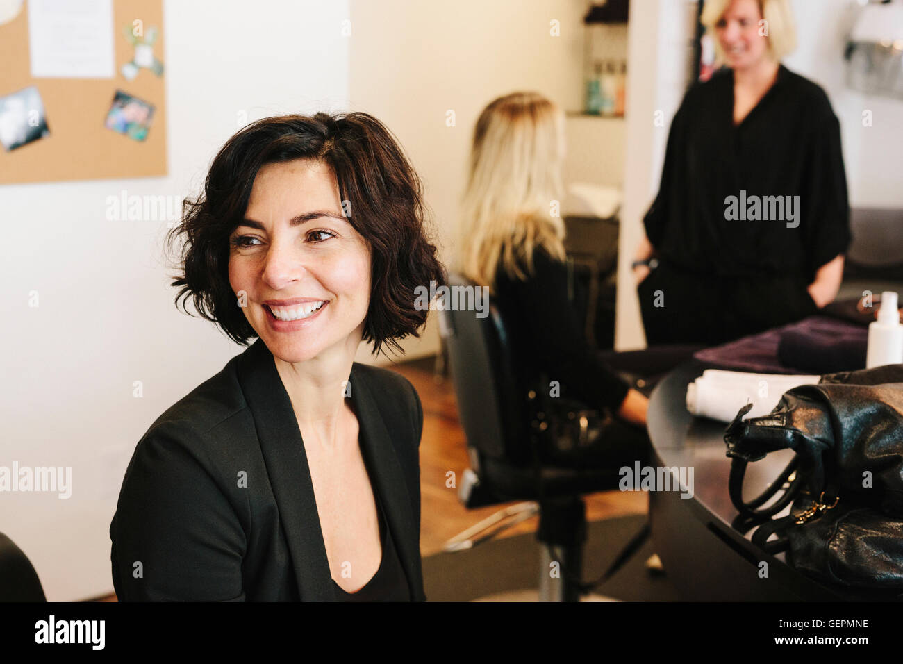Un client assis à un salon de coiffure, avec deux personnes à l'arrière-plan. Banque D'Images