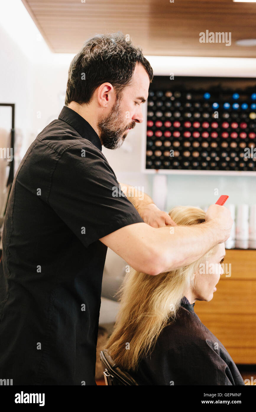 Un homme mûr, un coiffeur, coloriste, travaillant sur les cheveux d'une femme, l'application de couleur de cheveux au centre. Banque D'Images