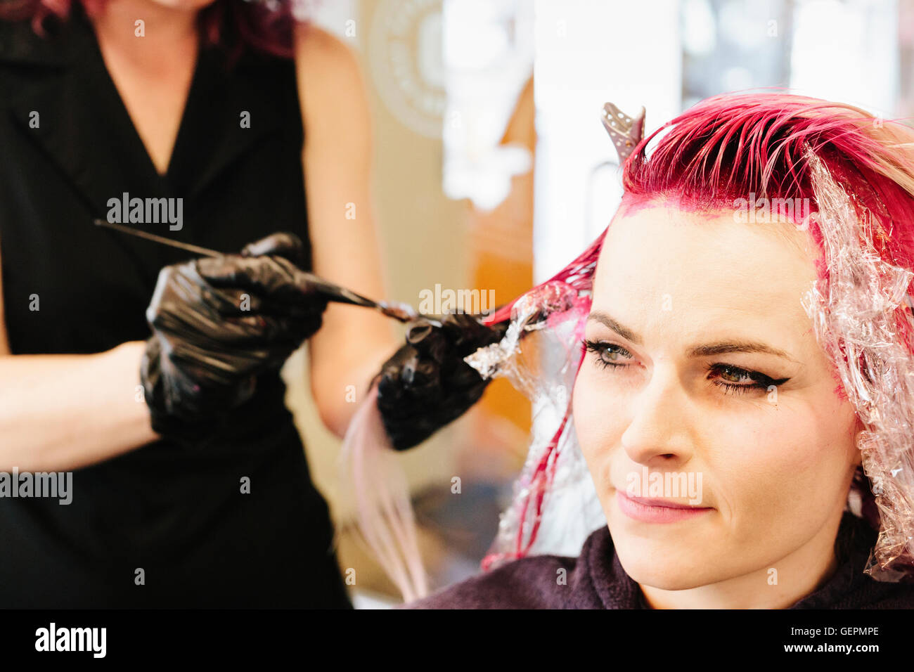 Une femme dans un salon de coiffure ayant une couleur de cheveux rose appliqué à ses cheveux blonds. Banque D'Images