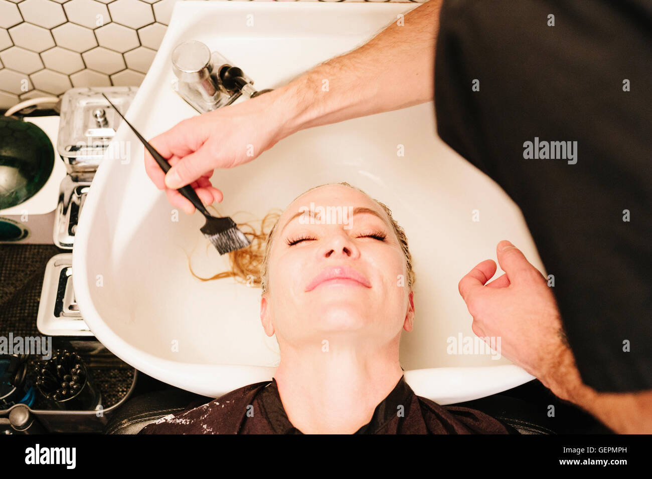 Une cliente à un salon de coiffure à le bassin ayant un traitement des cheveux appliqué avec un pinceau. Banque D'Images