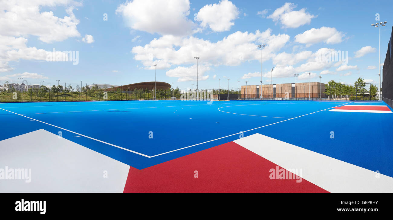 Terrain de hockey en bleu avec vue contextuelle vers Tennis Center et le vélodrome. Eton Manor - Lee Valley Hockey et Tennis Center, Londres, Royaume-Uni. Architecte : Stanton Williams, 2014. Banque D'Images