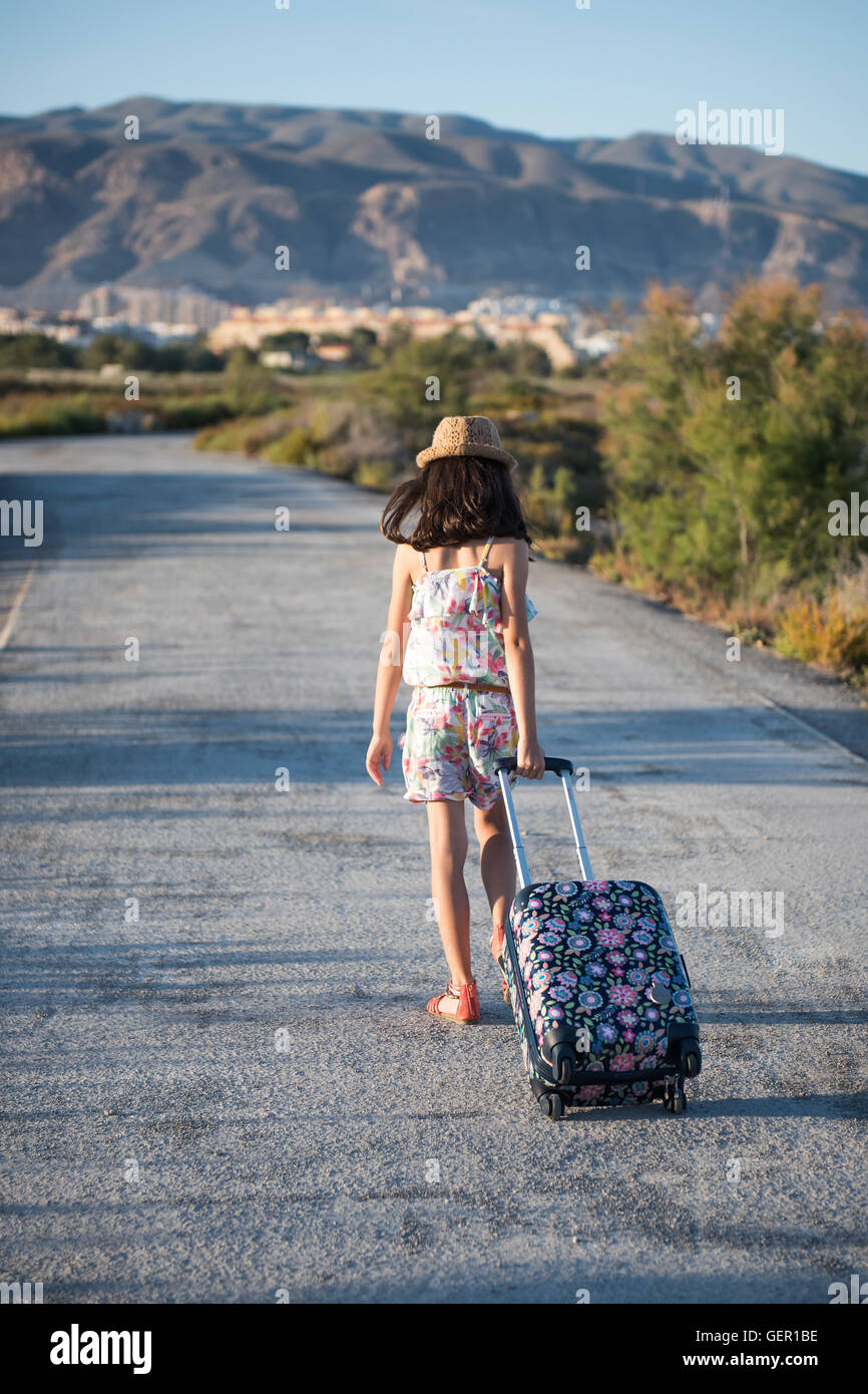 Belle jeune fille enjouée avec une valise marchant le long de la route Banque D'Images