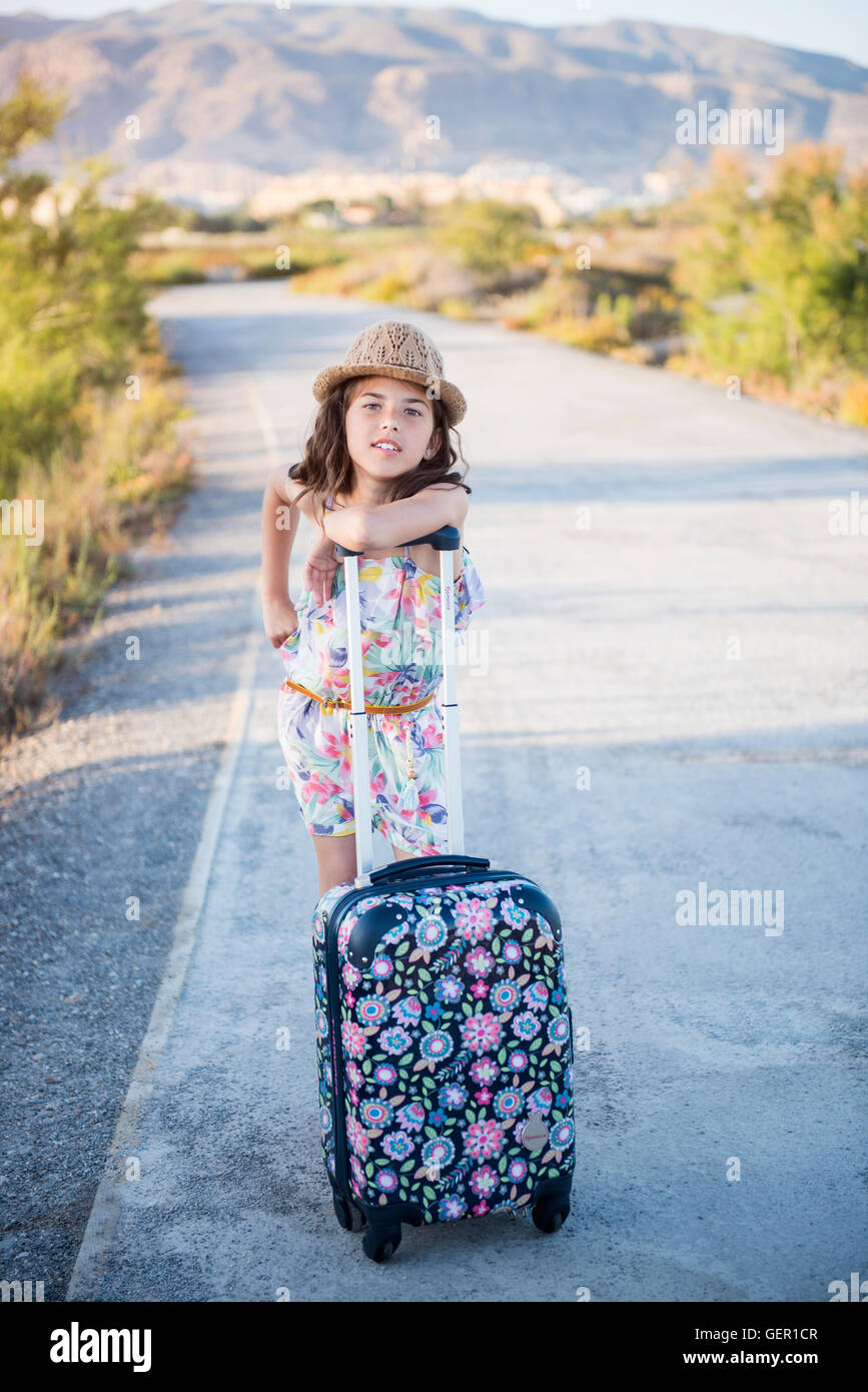 Belle jeune fille enjouée avec une valise marchant le long de la route Banque D'Images