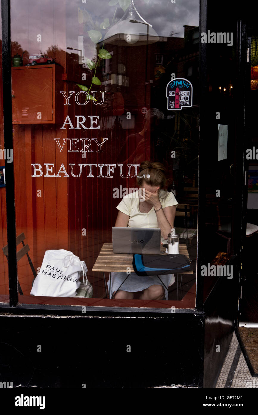 Une femme cache son visage avec sa main alors qu'elle travaille sur son ordinateur portable dans un café de Londres. Banque D'Images