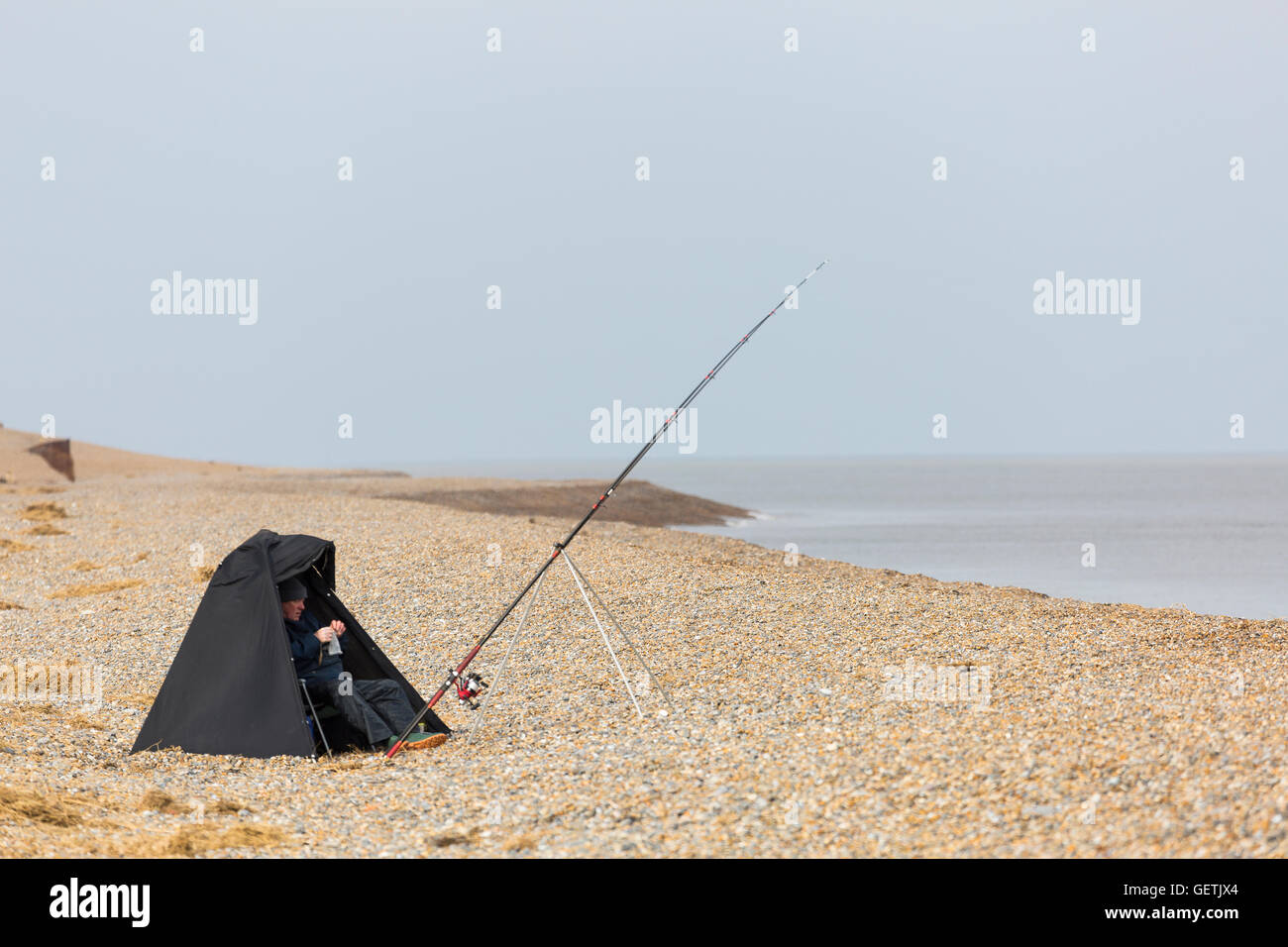 Plage de l'homme lors d'une journée de pêche avec un bivouac pour le protéger des éléments. Banque D'Images
