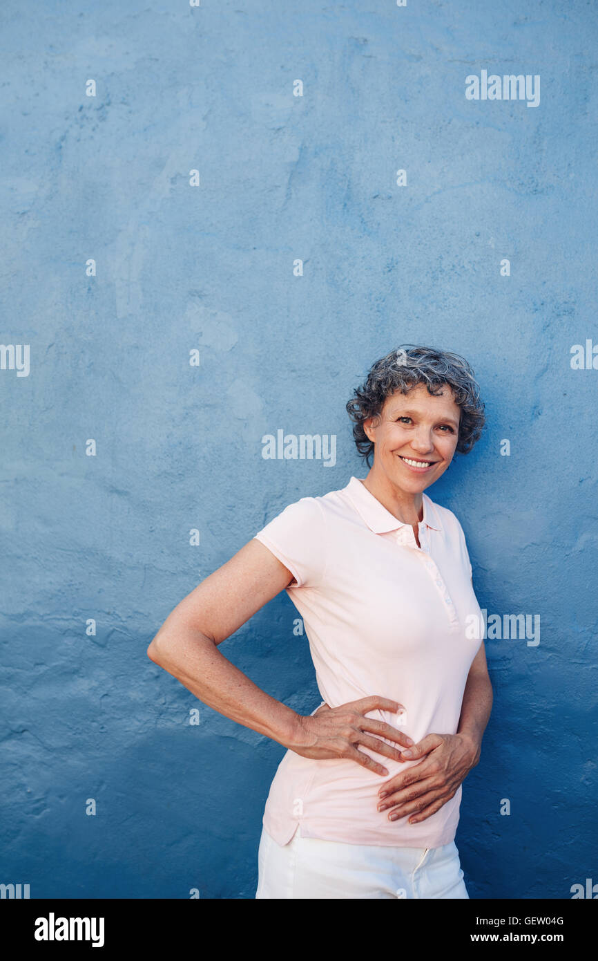 Portrait of attractive young woman posing à huis clos contre fond bleu. Les femmes d'âge moyen standing avec ses mains sur les hanches Banque D'Images