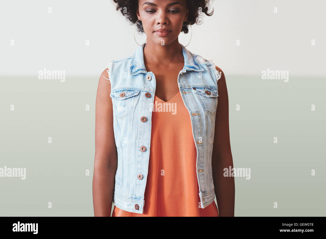 Image of young woman in stylish casuals debout contre un mur et à la recherche vers le bas. Femme africaine fashion model. Banque D'Images