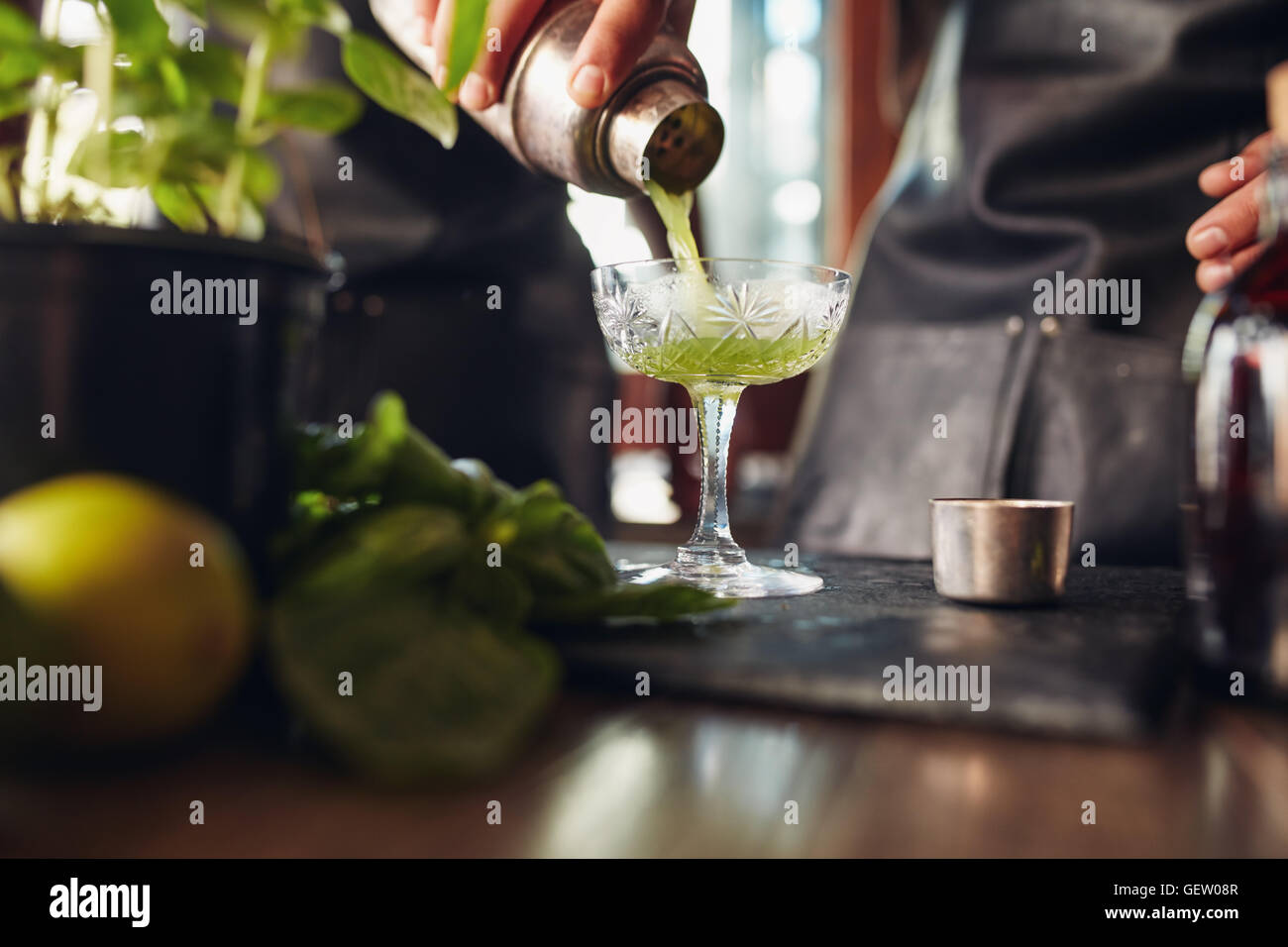 Gros plan de la main du barman pouring cocktail de basilic dans un verre d'agitateur. La préparation moderne barman classique smash basilic cockt Banque D'Images