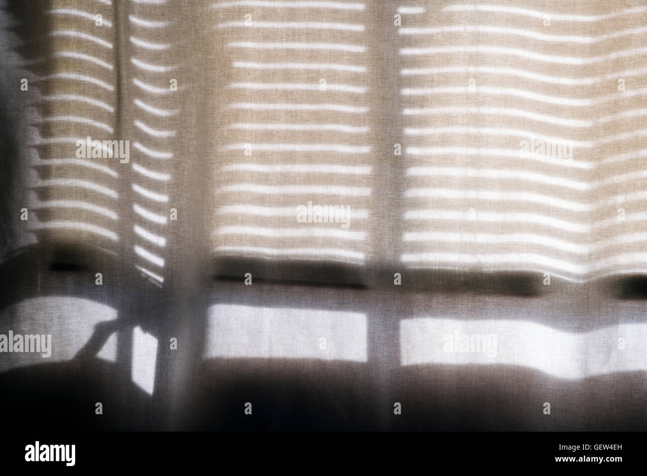 Les stores vénitiens cast un motif d'ombres sur un rideau de coton transparent. Banque D'Images
