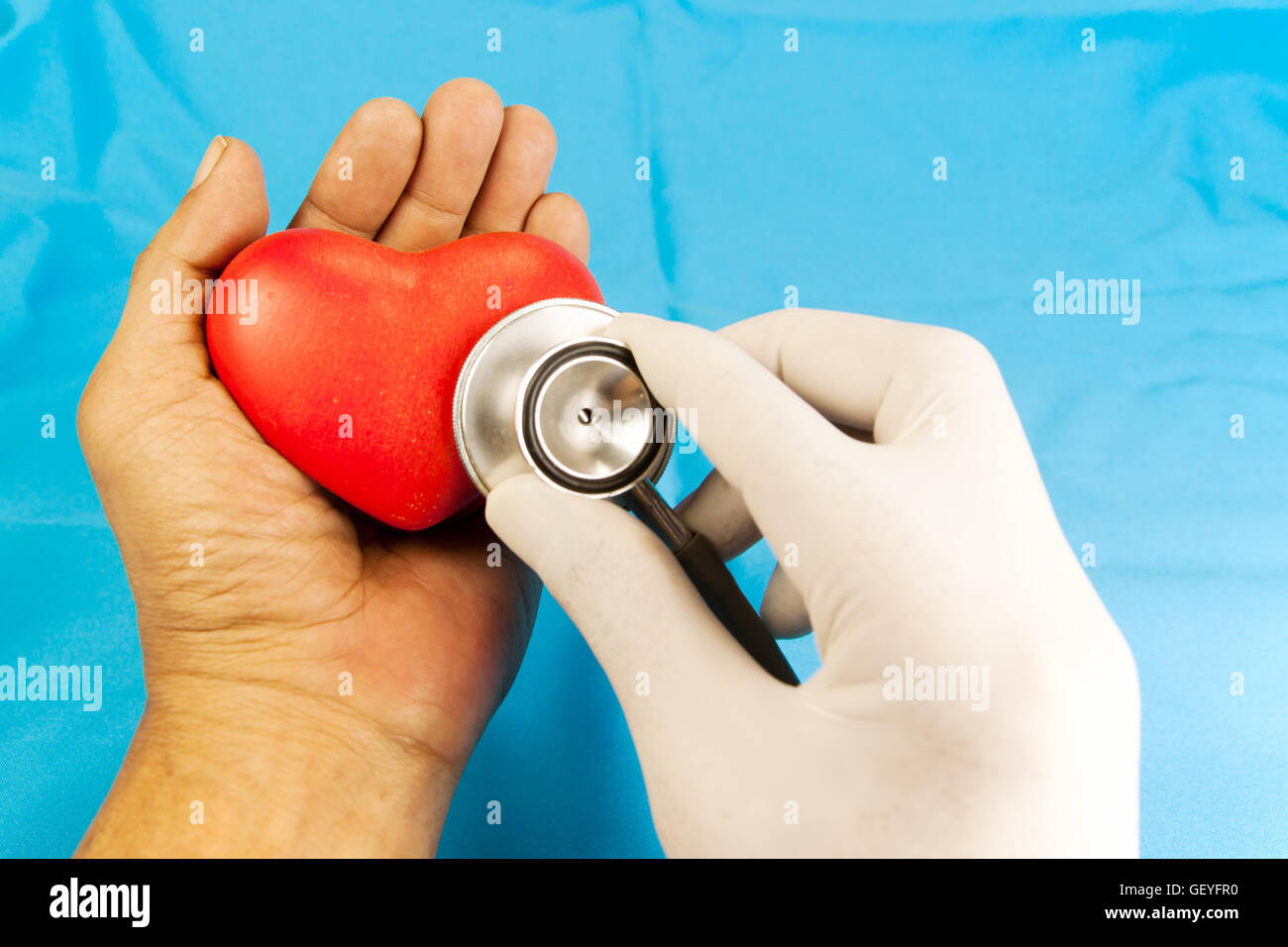Du coeur par stéthoscope. forme de coeur rouge dans la main sur fond de tissu bleu. Banque D'Images