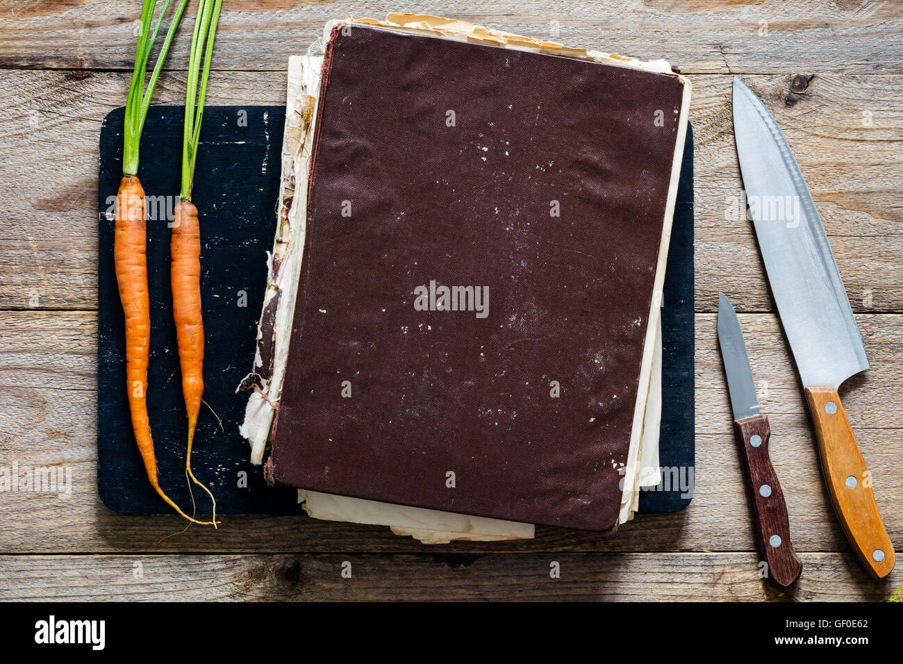 Vintage livre de cuisine avec des recettes santé sur planche à découper en bois. Deux jeunes carottes fraîches et deux couteaux de cuisine sur les côtés Banque D'Images
