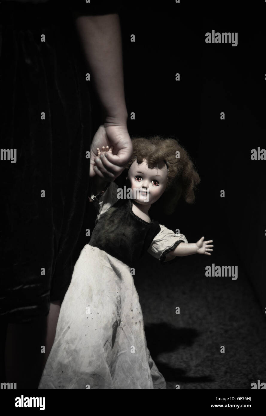 La main de l'enfant tenant une poupée avec des yeux lumineux effrayant. Banque D'Images