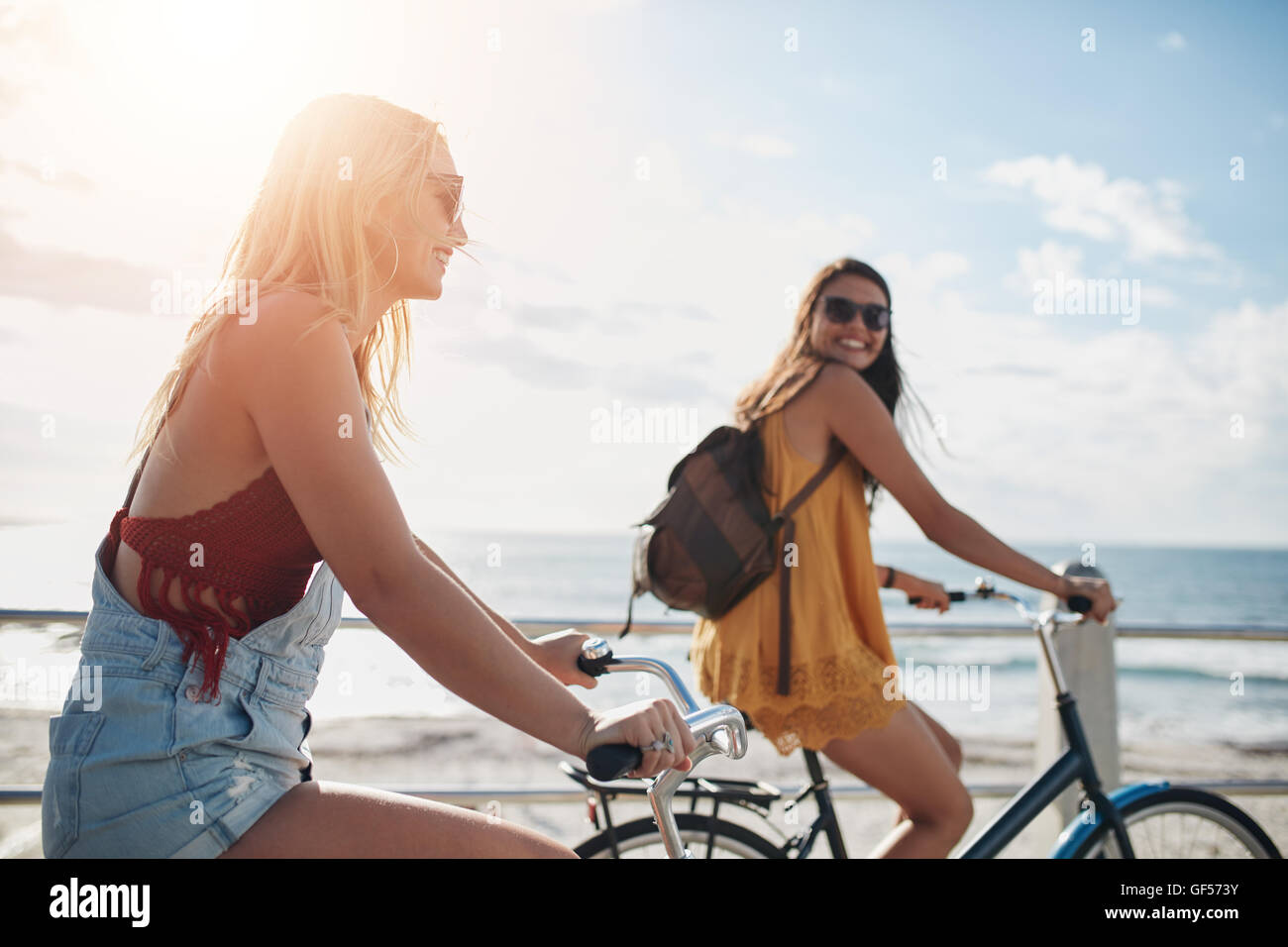 Deux amies équitation cycles sur la promenade du bord de mer. Heureux les jeunes femmes profitant de la bicyclette sur une journée d'été. Banque D'Images