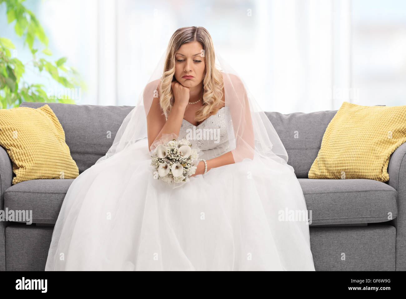 Enfoncé blonde bride sitting on a sofa et regardant vers le bas à la maison Banque D'Images