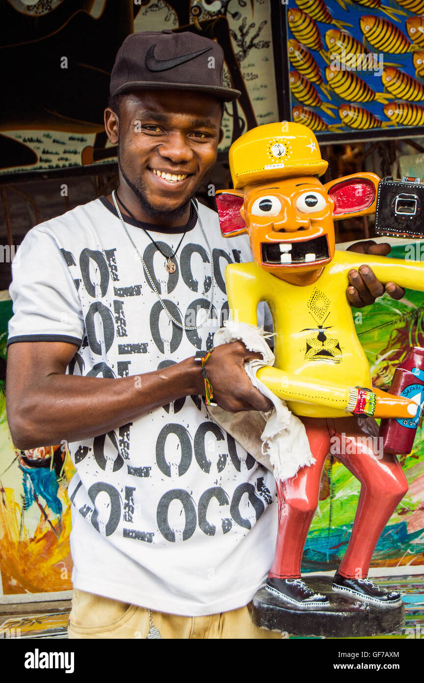 Homme avec Lilanga comic figure en bois peint de photographe en art shop, Centre Tingatinga, Dar-es-Salaam, Tanzanie Banque D'Images