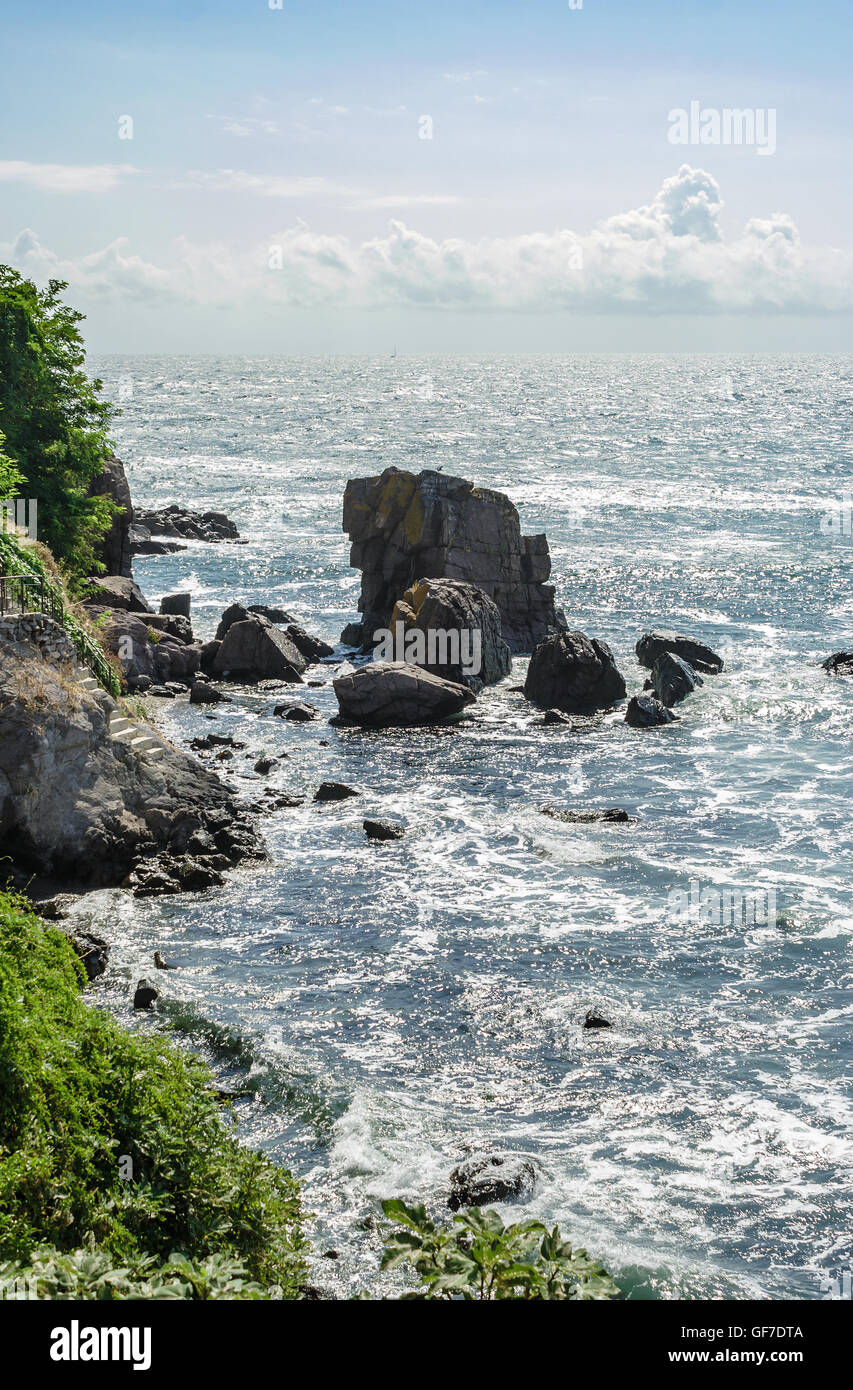 Mer vague attaque les rochers du rivage rocailleux et est rompu à leur sujet sur le lever du soleil Banque D'Images